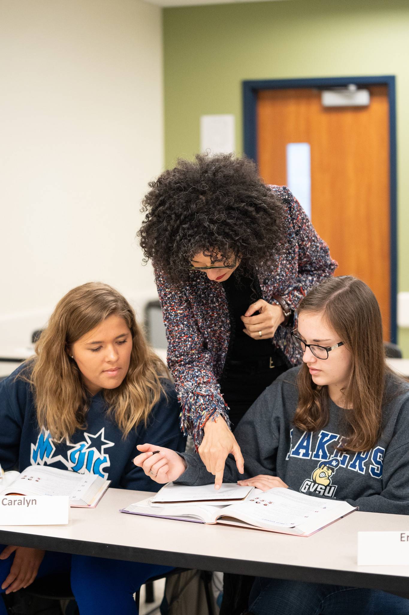 Two students seated at a table with an instructor between them, pointing at a text. Image by Amanda Pitts - University Communications